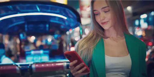 Forbes Casino — Hraj Online Kasino Pohodlně na Mobilu Mladá žena s telefonem v ruce používá mobilní aplikaci Forbes Casino v nočním městském prostředí.